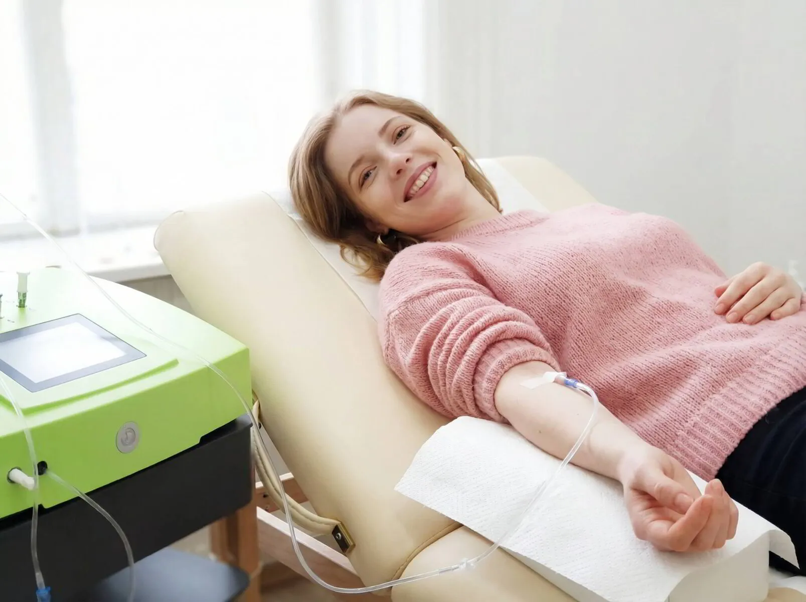 Lächelnde Patientin auf einer Behandlungsliege mit Infusionszugang am Arm während einer Ozontherapie, neben ihr das Ozon-Behandlungsgerät